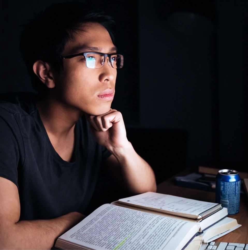 Concurseiro estudando de madrugada, pensativo diante do livro aberto